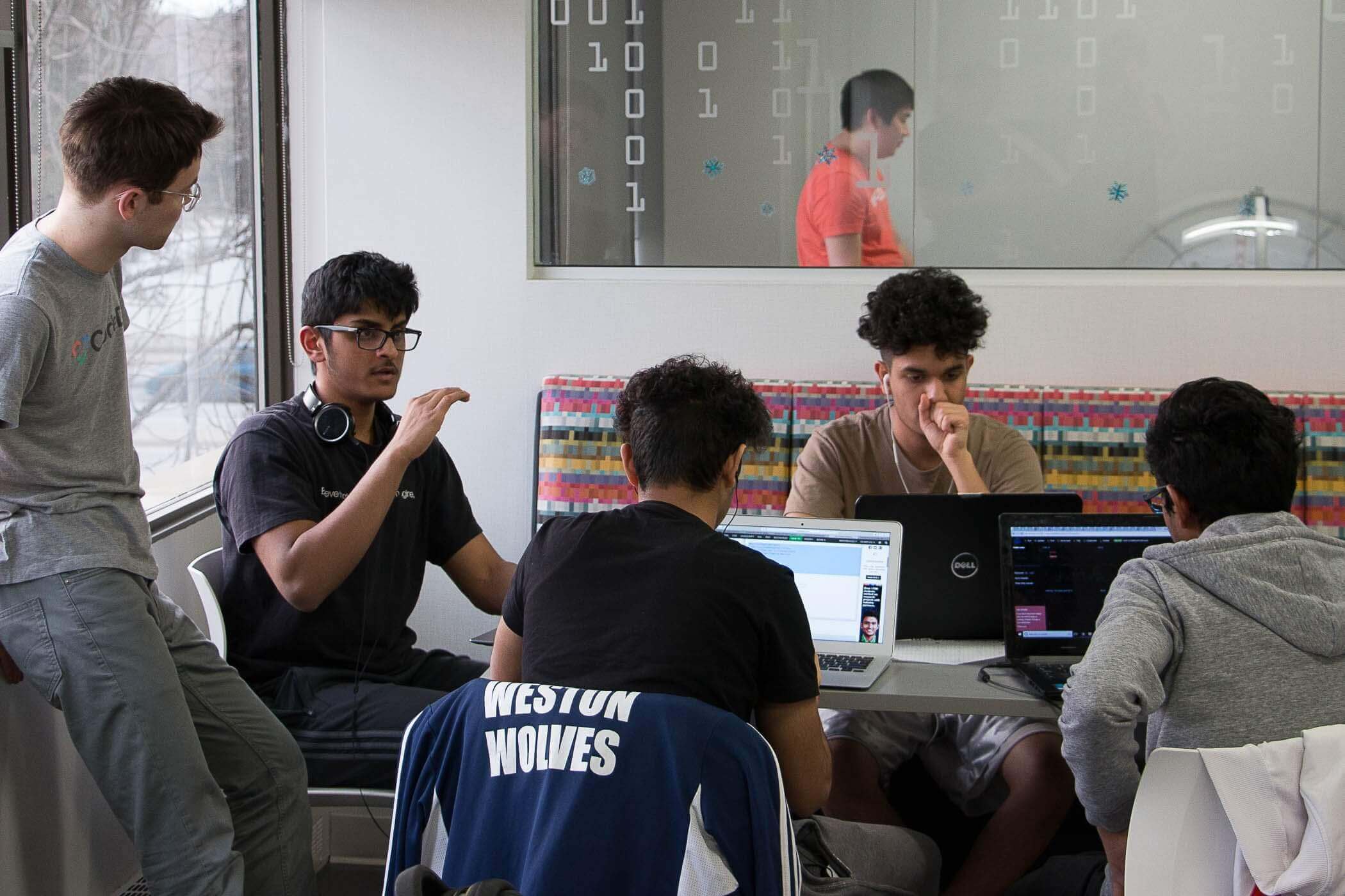Students are gathered at a table busy coding.