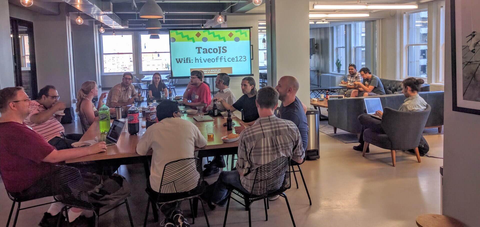 A small audience of 10 people sitting at a table eating Tacos